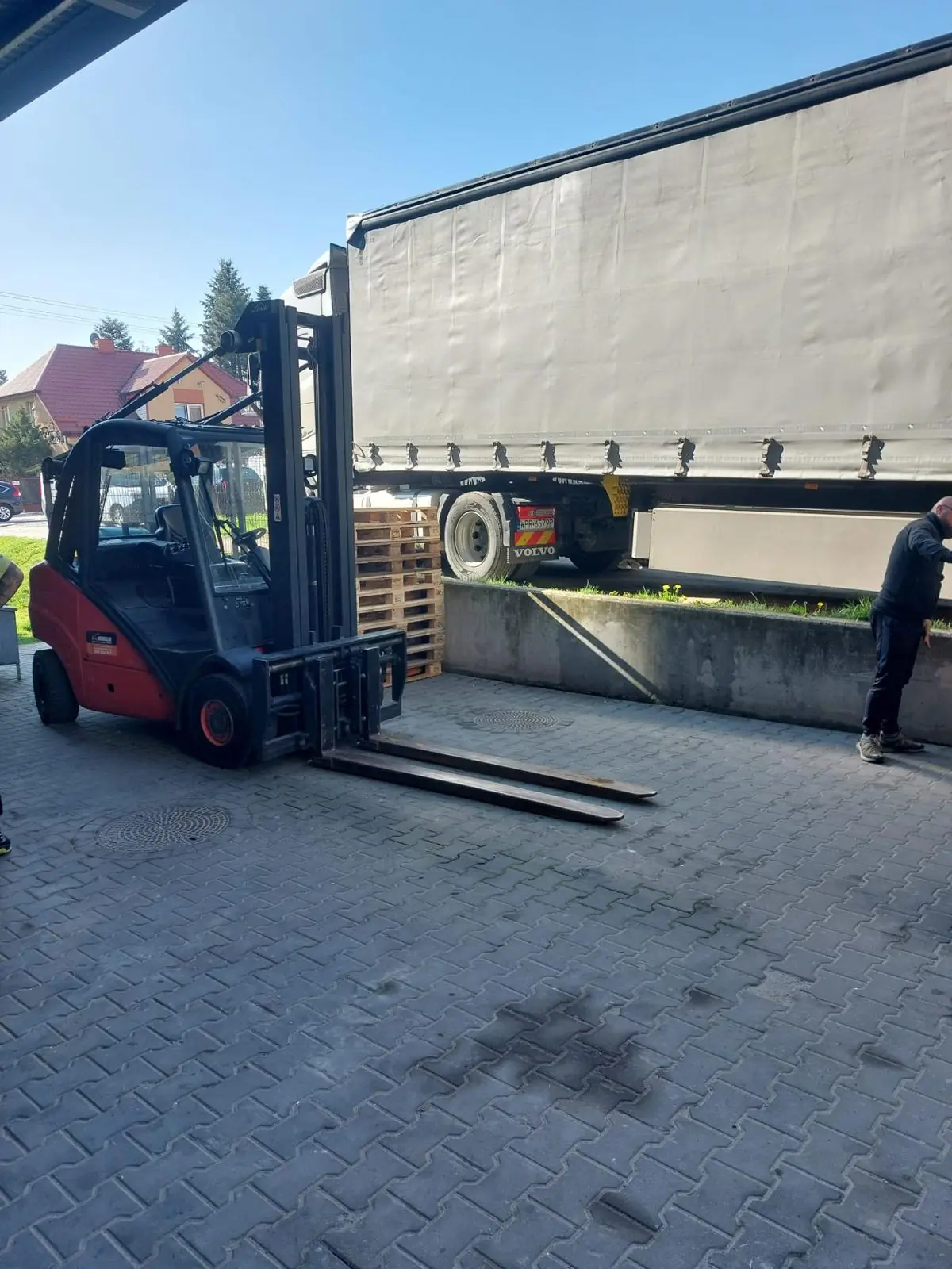 Rozładunek naczepy wózkiem widłowym Linde przy zestawie Volvo pod wiatą magazynu