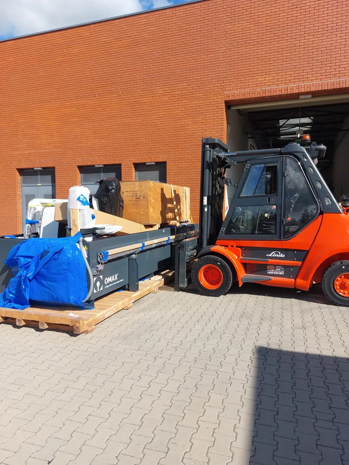 Transport przecinarki wodnej OMAX – rozładunek wózkiem widłowym Linde przed halą produkcyjną