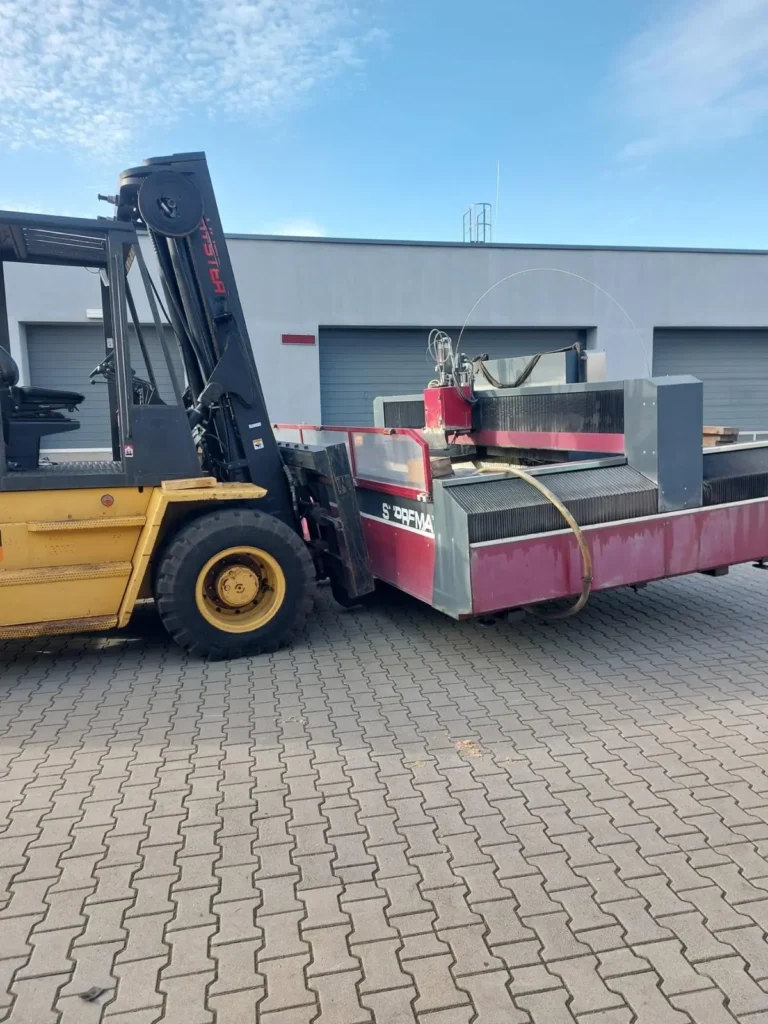 Transport przecinarki wodnej – wózek widłowy Hyster przewozi maszynę strumieniowo-ścierną przed halą